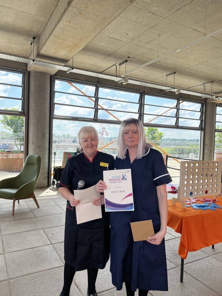 Lady smiling next to a lady who is holding a certificate