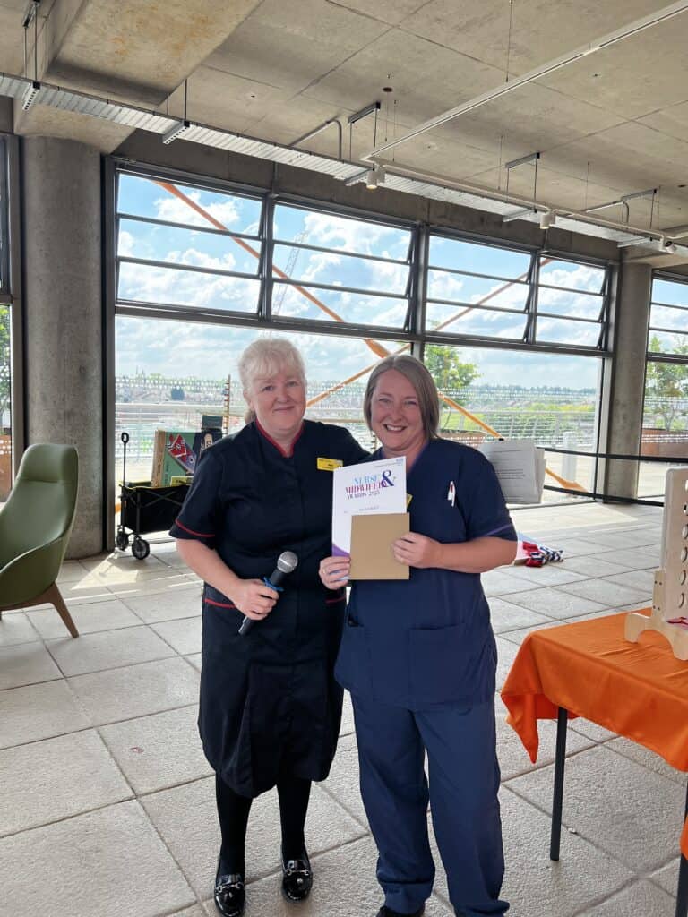 Lady smiling next to a lady who is holding a certificate