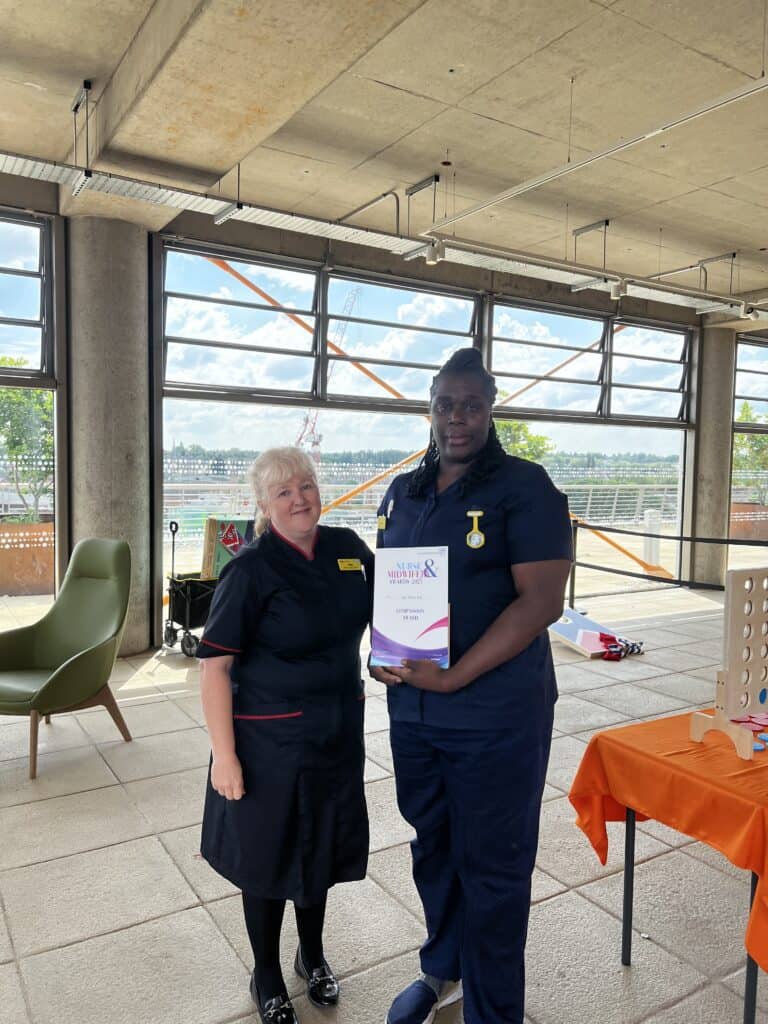 Lady smiling next to a lady who is holding a certificate