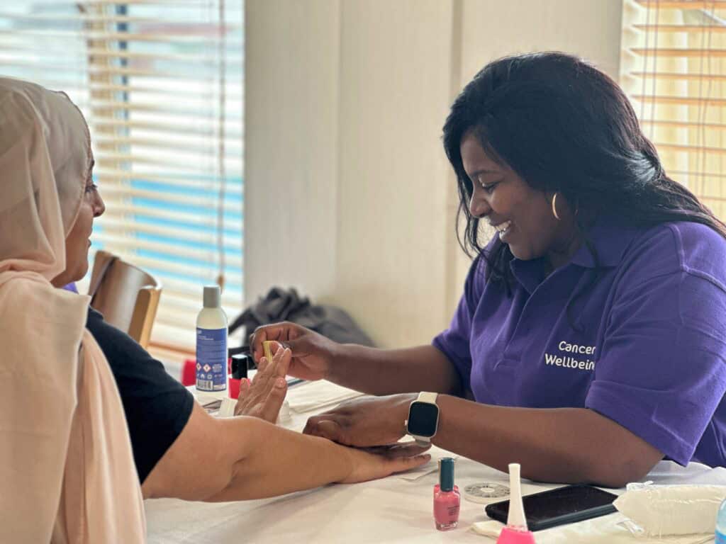 A lady in a purple polo shirt painting a women's nails.