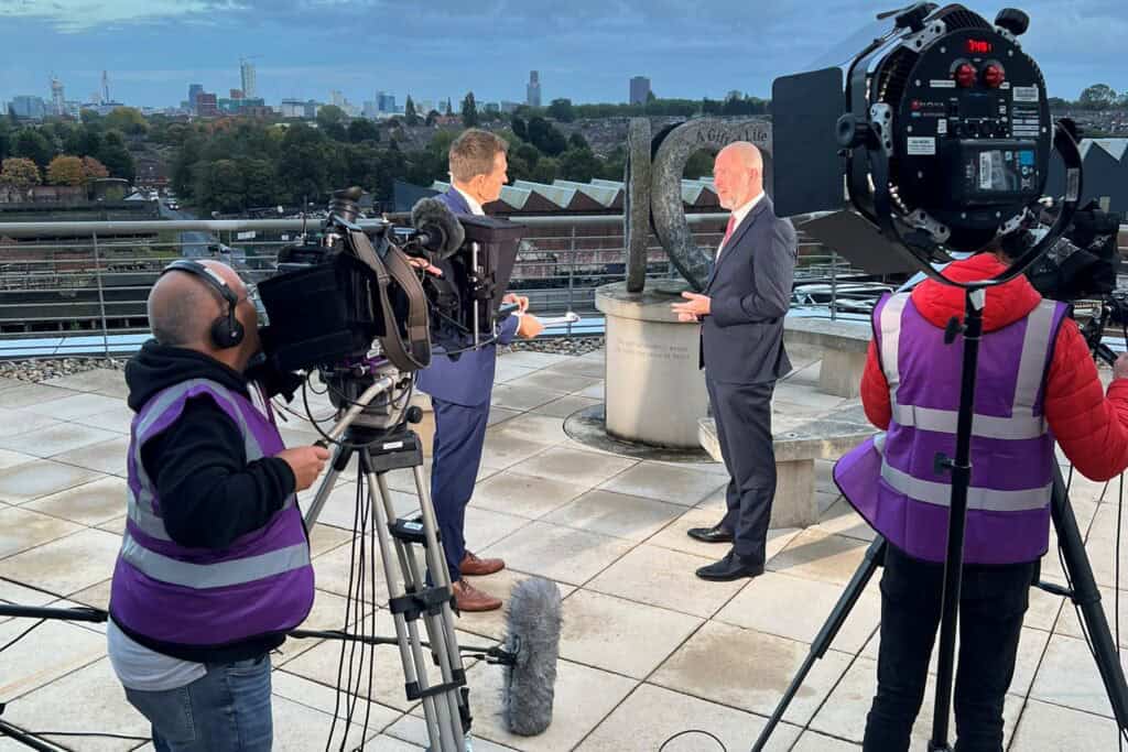 Film crew filming a live news broadcast on a hospital balcony