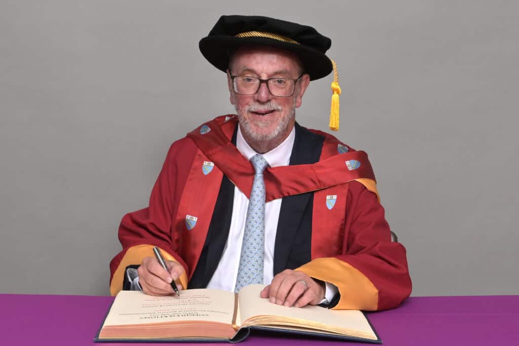Trust chairman in academic gown signing a book
