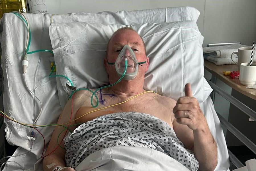 An image of a man in a hospital bed with an oxygen mask on. He is doing a thumbs up to the camera.