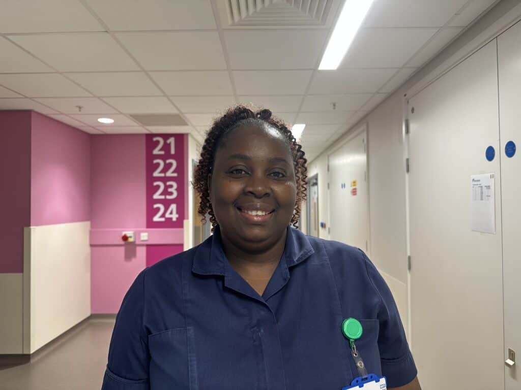 A smiling nurse standing in a hospital corridor in uniform.