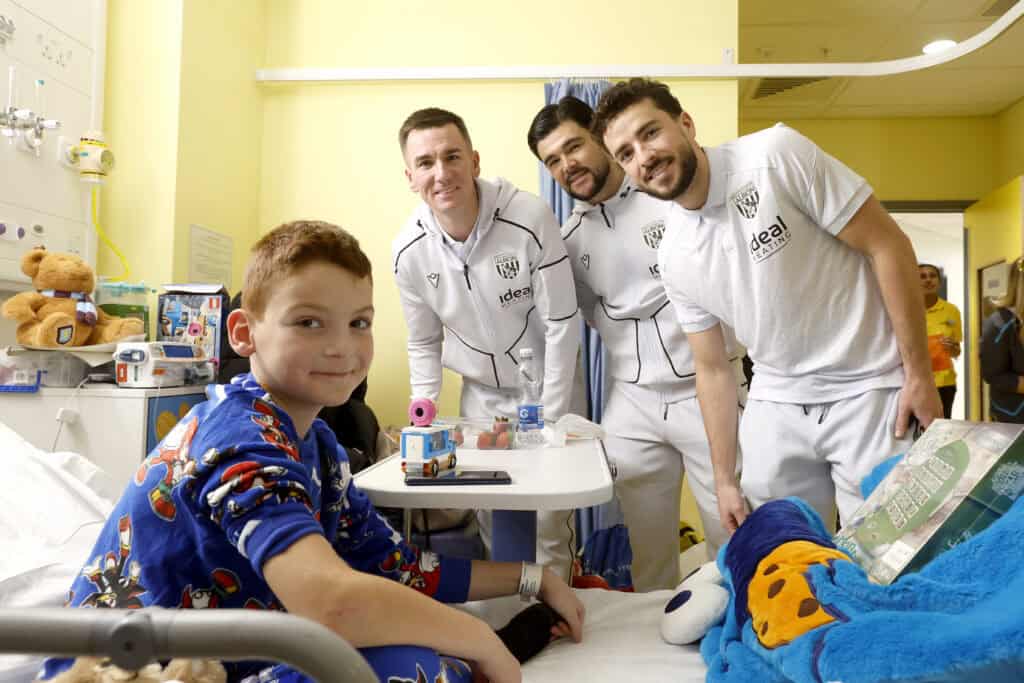 Three football players from West Bromwich Albion at a young patient's bedside in hospital.
