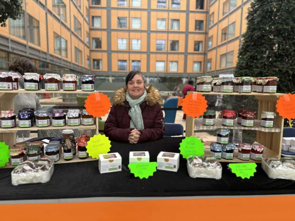 A photo of a lady on a market stall selling jams and chutneys.