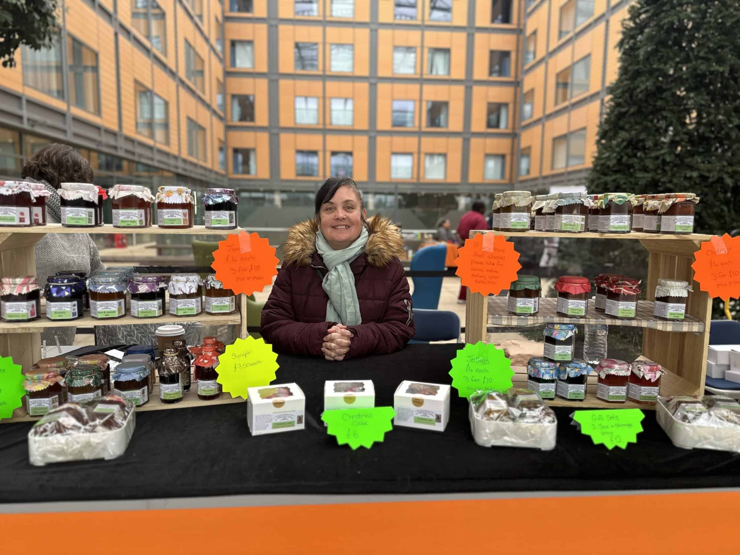 A photo of a lady on a market stall selling jams and chutneys.