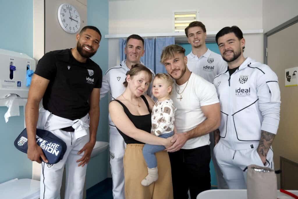 Football players from West Bromwich Albion posing for a photo with a two-year-old and his parents in hospital.