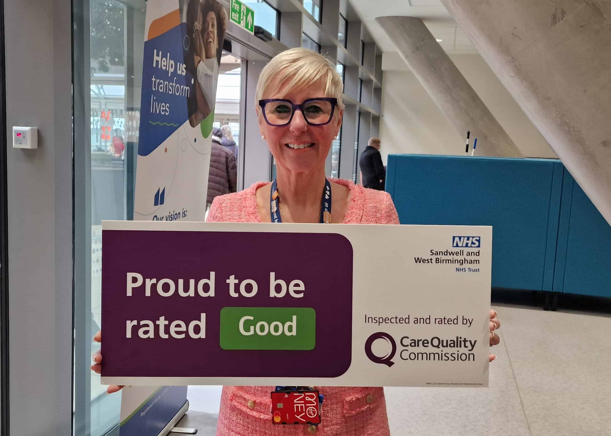 A picture of Diane Wake holding a board that says "Proud to be rated Good."