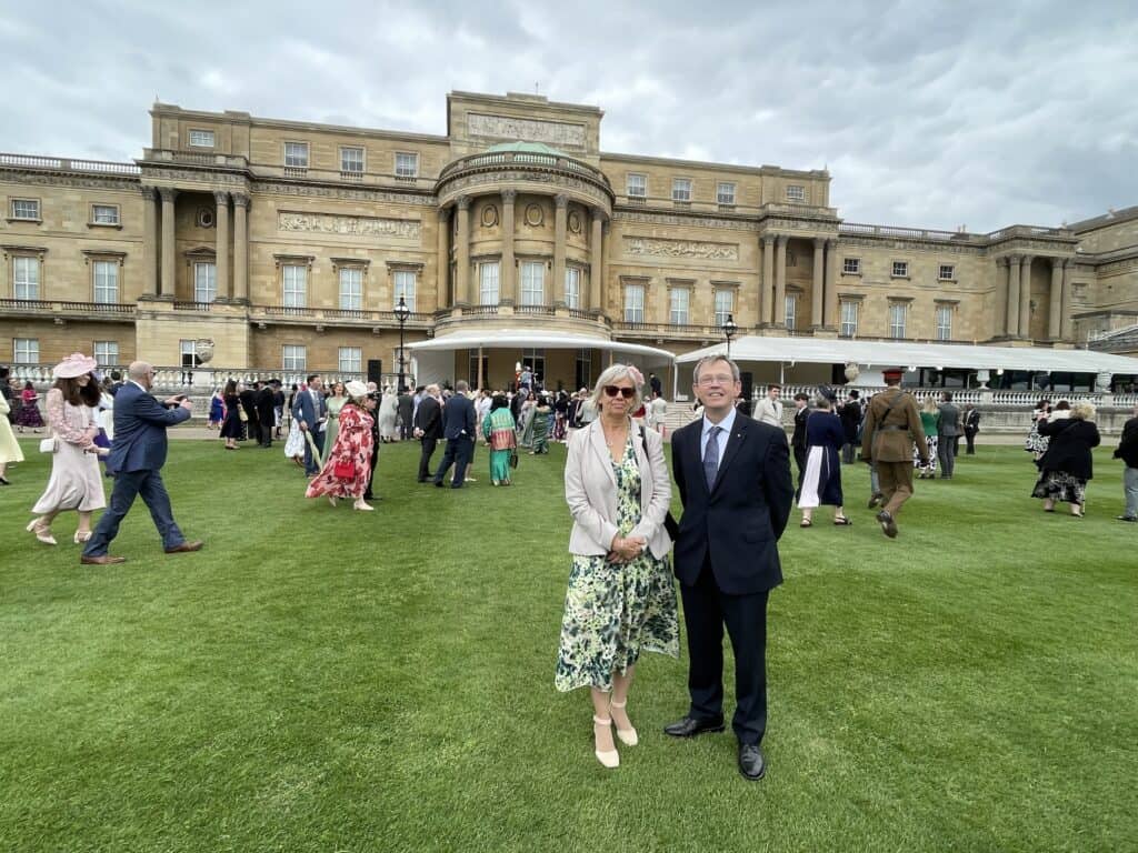 A photo of a man and woman in black tie clothing, in the gardens of Buckingham Palace.