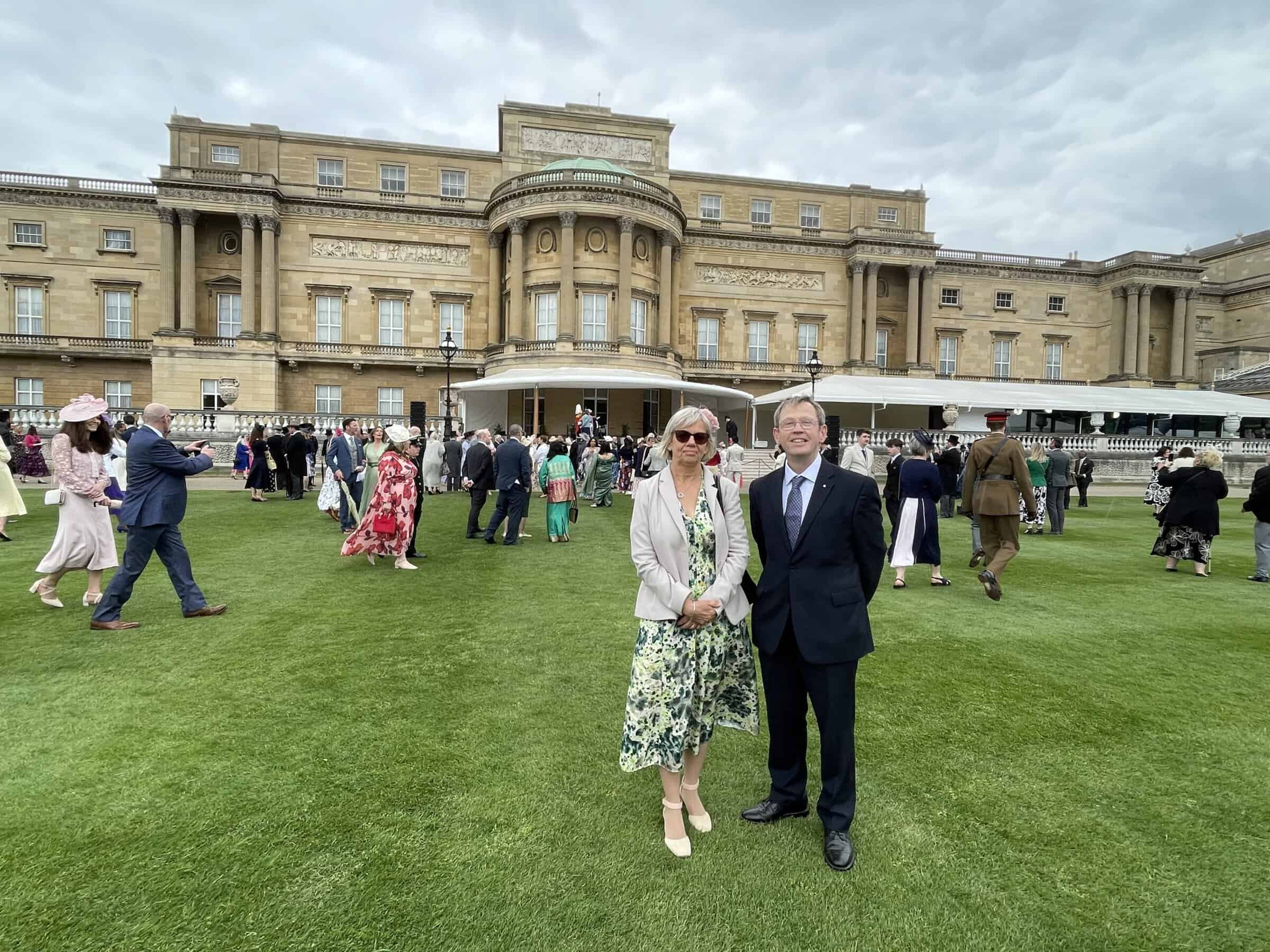 A photo of a man and woman in black tie clothing, in the gardens of Buckingham Palace.